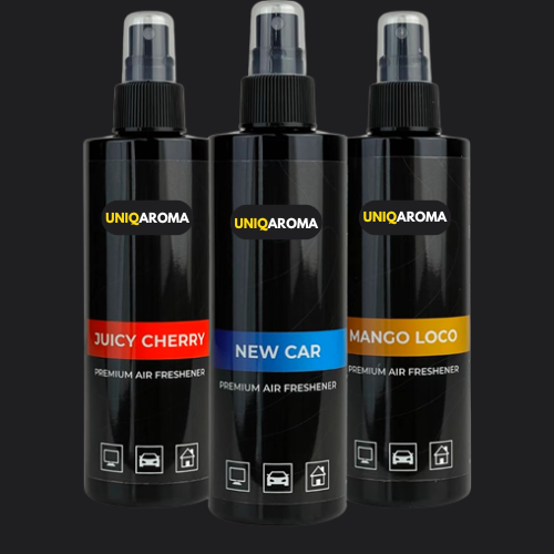 Three black bottles of UNIQAROMA air freshener, featuring 'Juicy Cherry' with a red label, 'New Car' with a blue label, and 'Mango Loco' with a yellow label. Each bottle has a white logo and text identifying them as 'Premium Air Freshener' with icons for car, office, and home use.